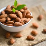 Almonds nuts on white bowl and green leaf on sack backgroundม, Delicious sweet almonds on the wooden table, roasted almond nut for healthy food and snack