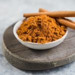 Ceylon cinnamon sticks with cinnamon powder in wooden bowl on concrete background.